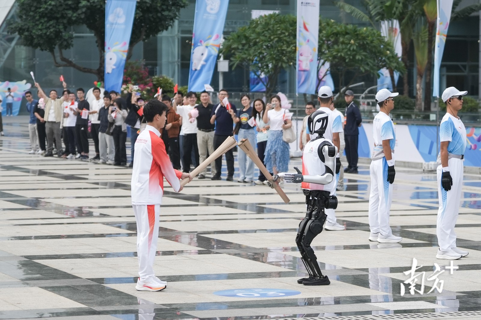 第十五届全国运动会深圳站火炬传递活动现场，“0号”火炬手人形机器人“夸父”向“手搓火箭”的高中生王裕宁传递火炬